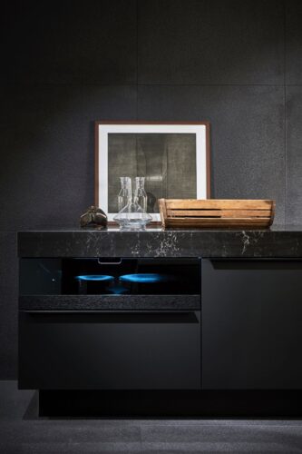 Dieses Premium-Wohnküchen-Design setzt anstelle von Glasschränken auf extravagante Vitrinenauszüge als „Schaukasten“ – ein tablettartiger Auszug aus Holz, der mit einem dunklen Glaskubus veredelt ist. Foto: AMK