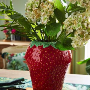 Blumen machen den gedeckten Tisch erst komplett. Aktuell sehr angesagt sind Vasen in Form von Früchten. So auch die rote Keramik-Erdbeervase, die einen schönen Kontrast zu den weißen Hortensien bildet, von Joe Browns.