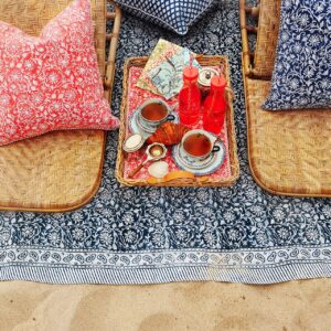 Ein Strand-Picknick mit ganz elegantem Charakter, das ist mit den Textilien im französischen Stil von Chamois garantiert. Die niedlichen Muster wirken verspielt und harmonieren in Blau und Koralle perfekt miteinander. Besonders praktisch sind auch die Rattanstühle, an die man sich bequem anlehnen kann.